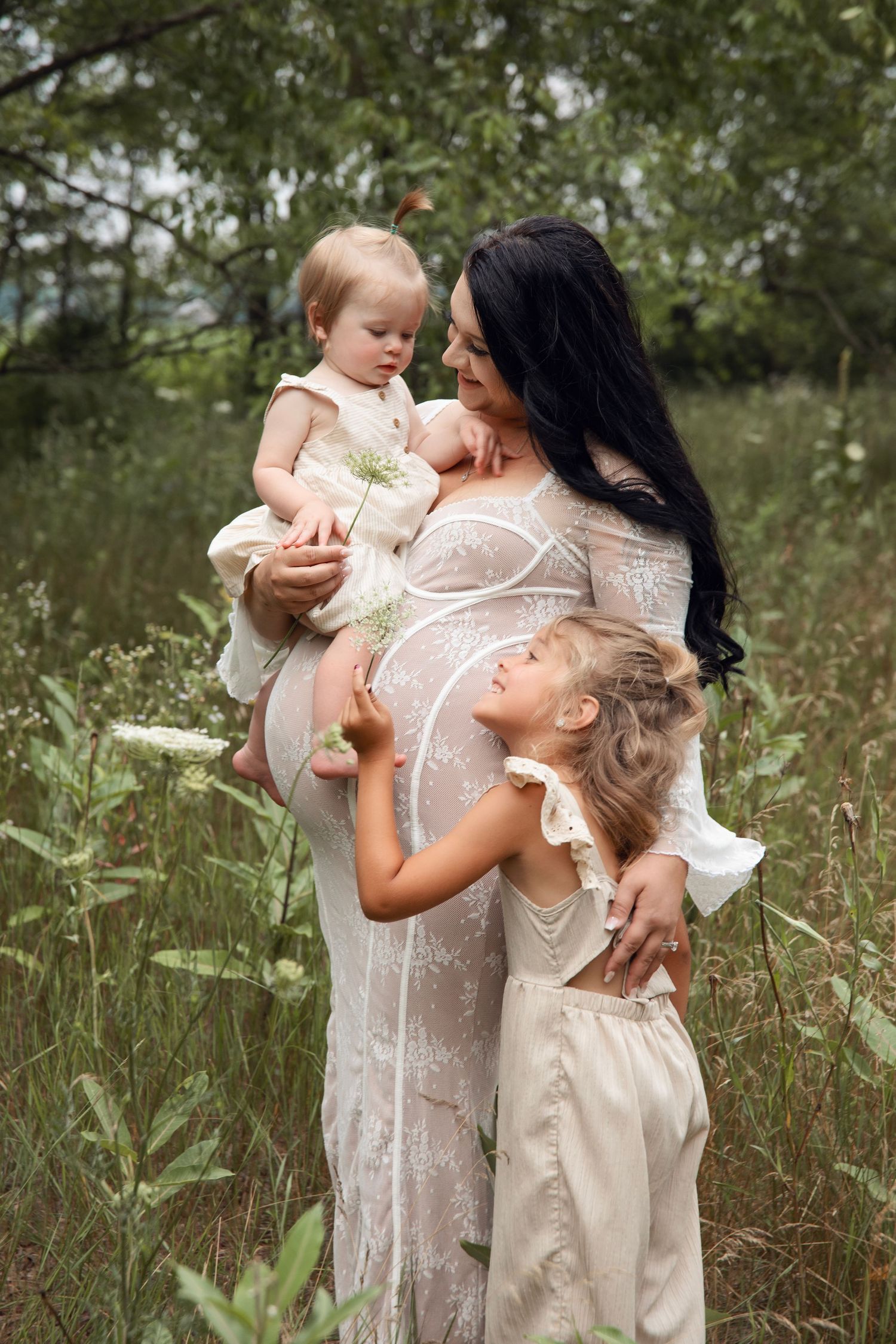 Family wearing cream and white lace dresses pose together in a wildflower meadow on a summer day.