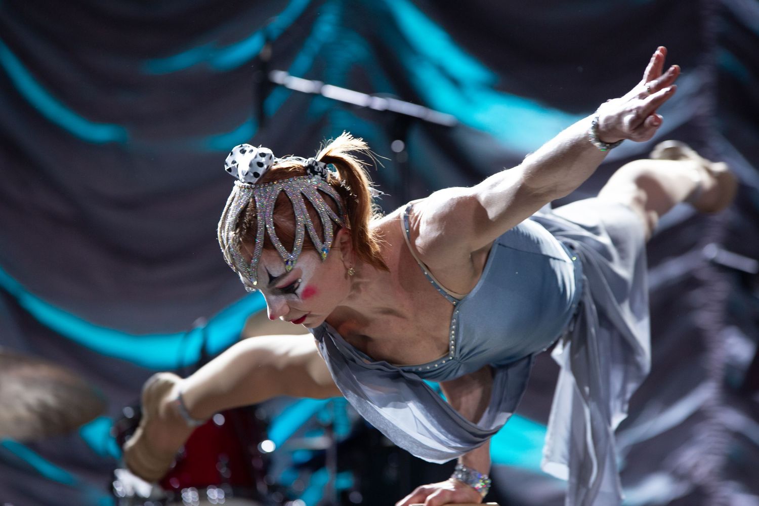Circus dancer performs dynamic contemporary dance move against turquoise background during theatrical performance.