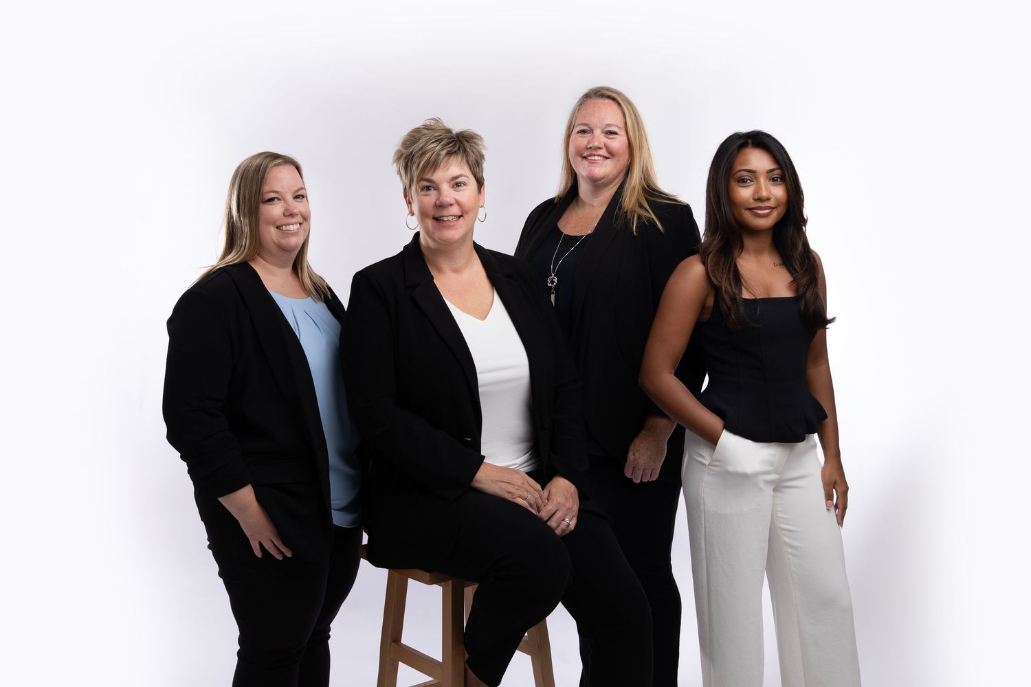 Four professionals in business attire pose together against a white studio background.