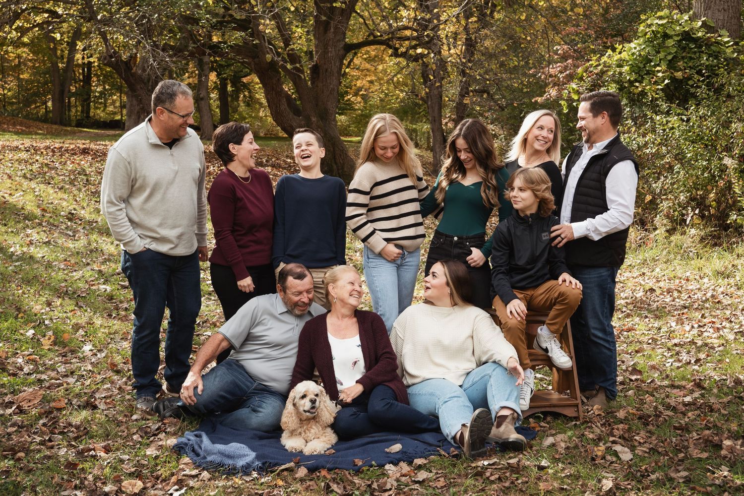Extended family group poses together on ground with dog in autumn forest scene.