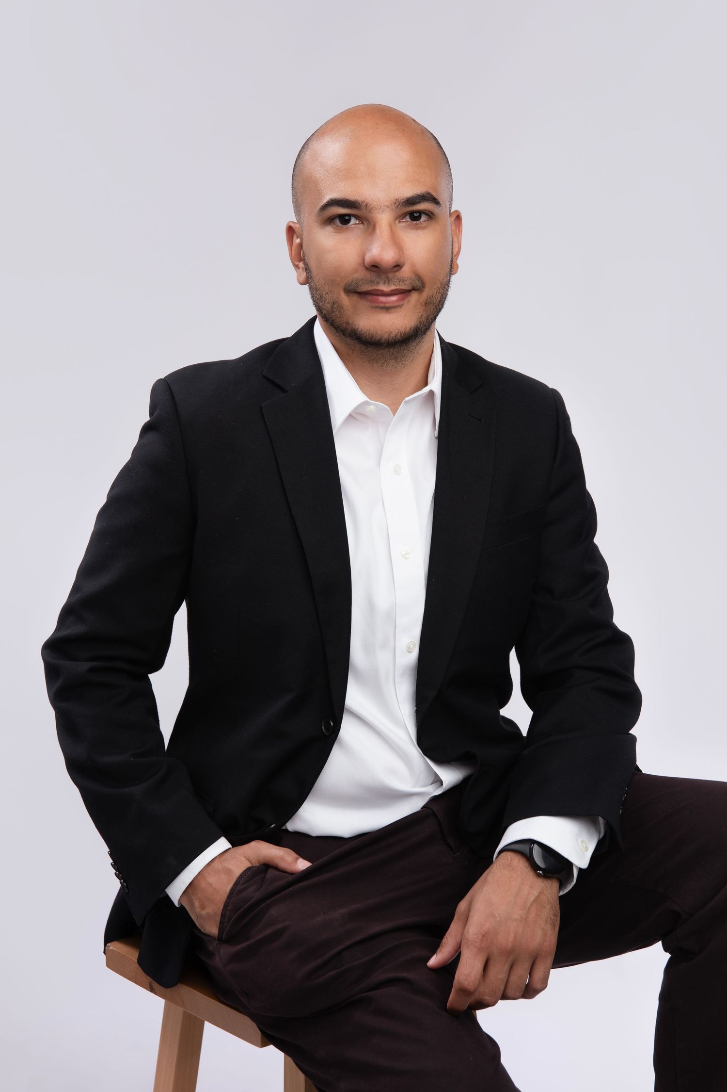 Professional studio portrait of a person in a black blazer and white shirt against a light gray background.
