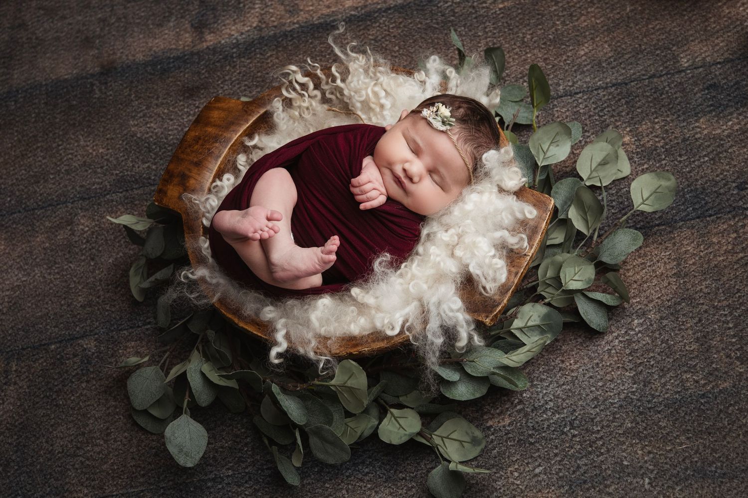 Artistic newborn photography with baby nestled in dark textured setting with greenery.