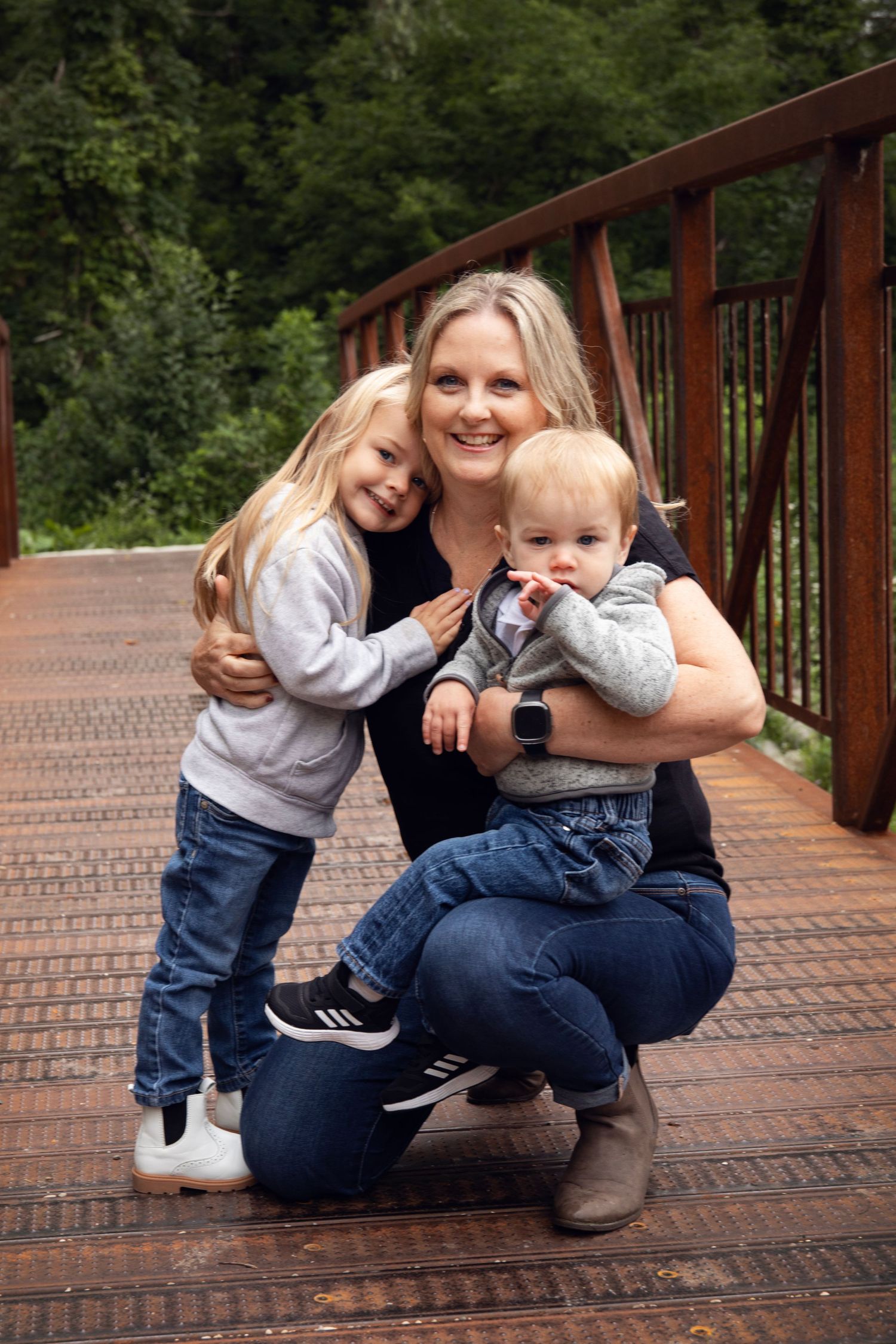 Parent and child share playful moments on wooden bridge in forest setting.