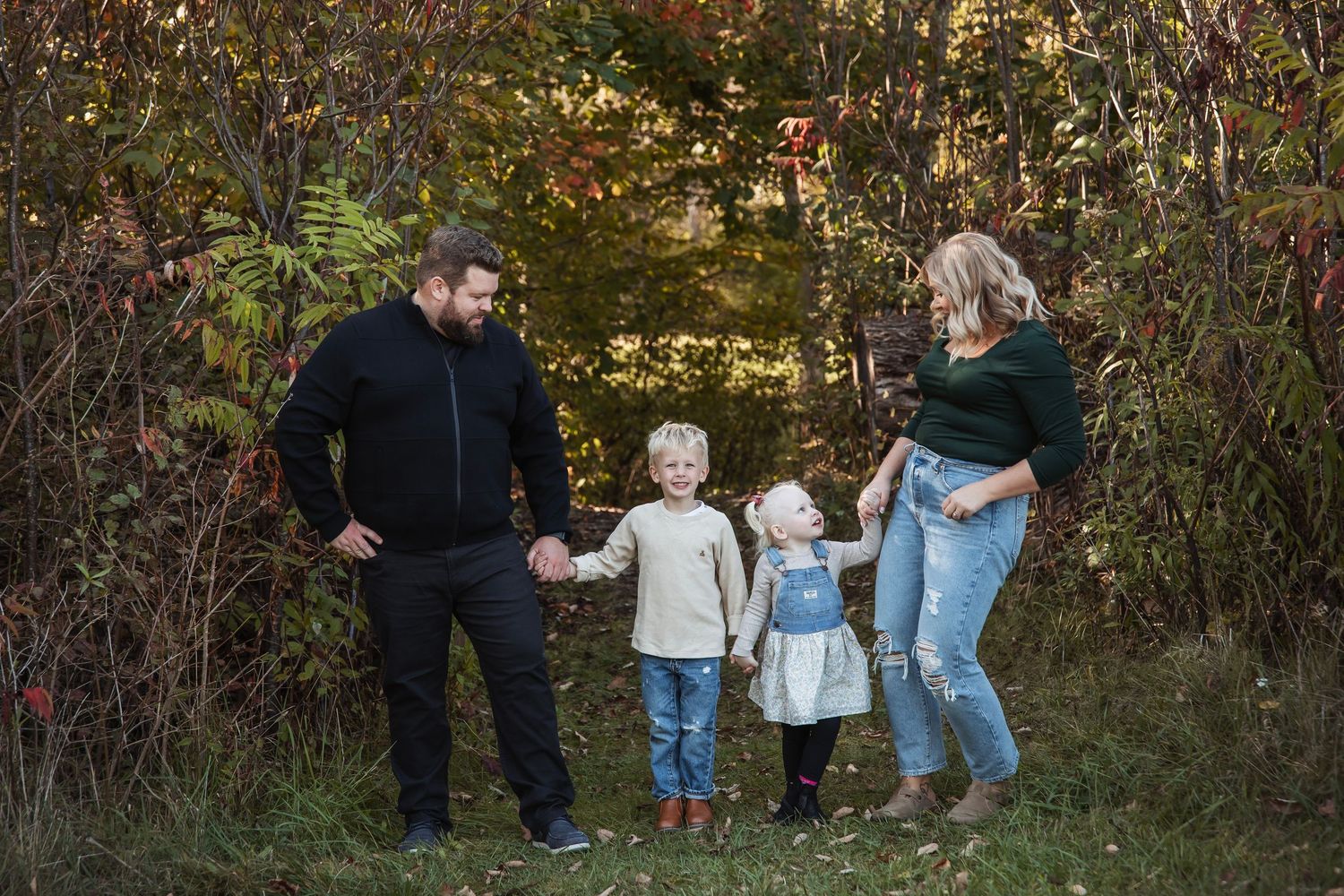 Family playing and laughing together at edge of wooded area during sunset.