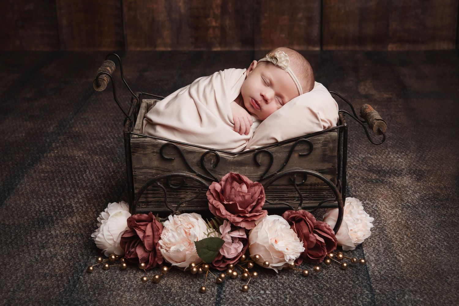 Sleeping newborn in white wrap surrounded by vintage decor and burgundy flowers.