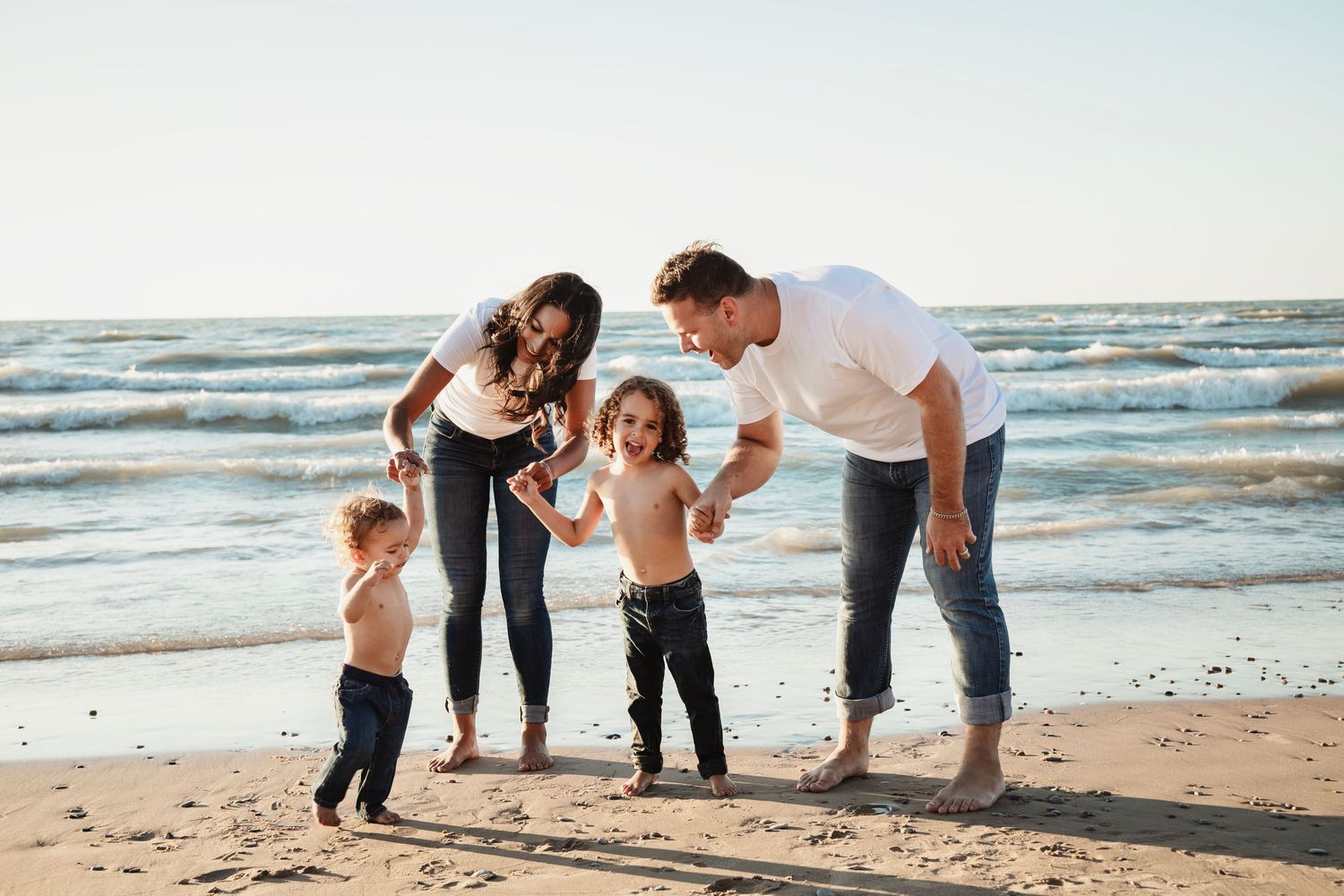 Family playing and interacting together on sandy beach with ocean waves in background.