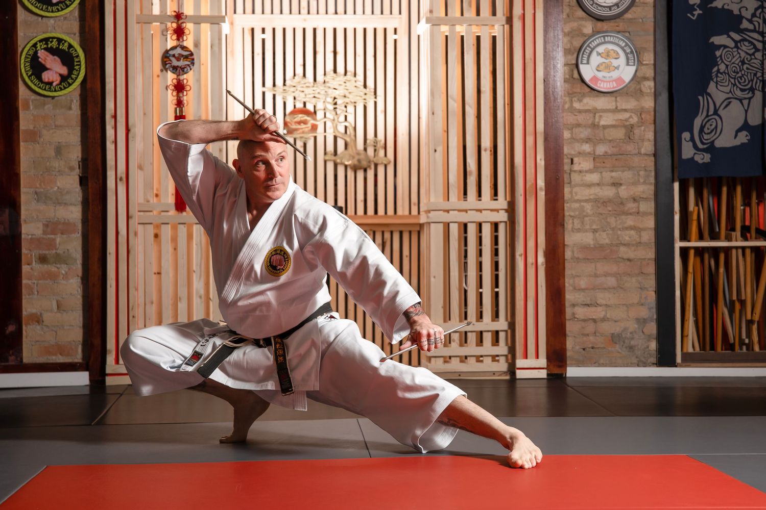 Karate martial artist in white gi performs a low stance with a sword in a traditional dojo setting.