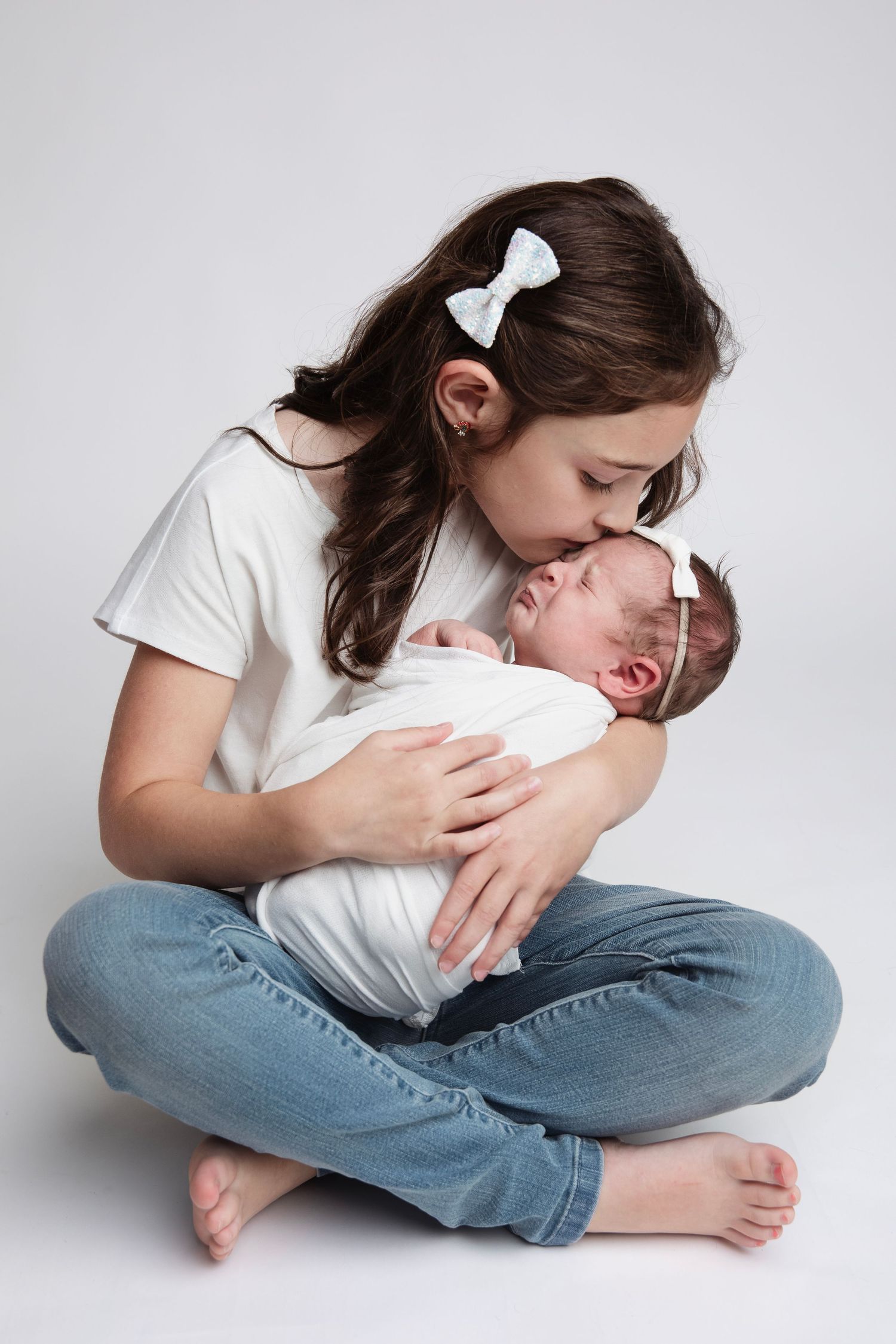 Young girl in white shirt and jeans tenderly cradling newborn sibling.