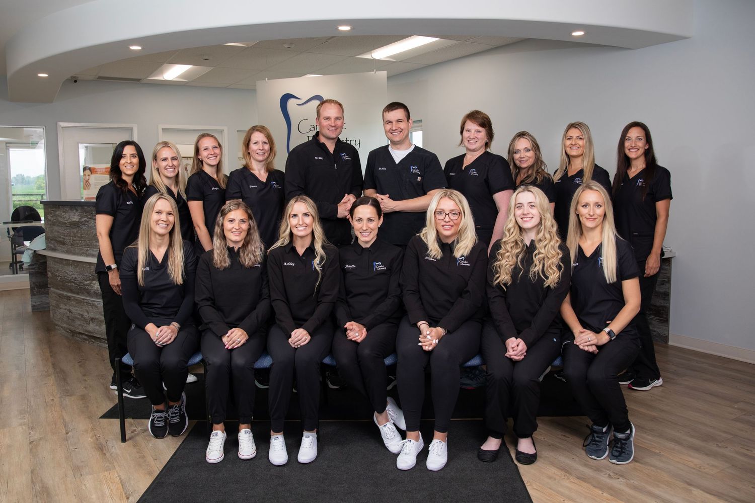 A professional medical or dental office staff wearing matching black uniforms poses together for a group photo.