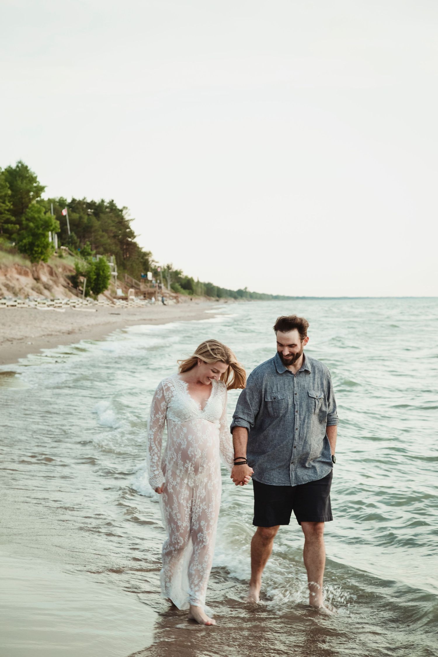 Two people stand together in shallow ocean water along a scenic coastal beach.