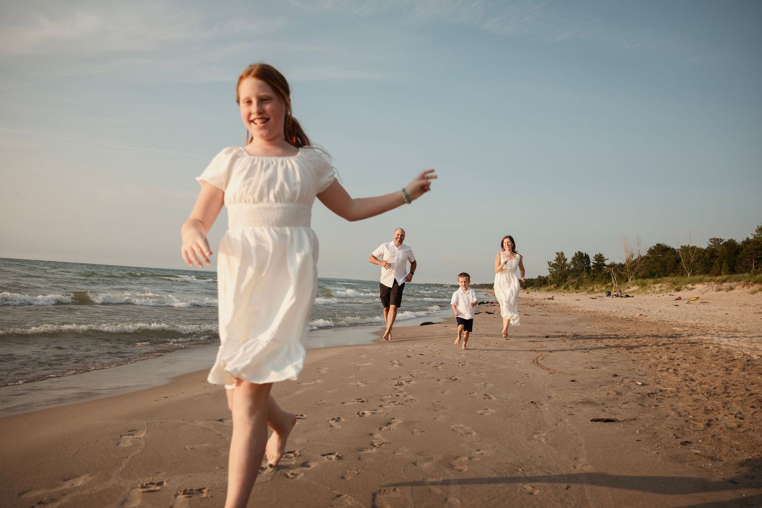 People running and playing together on a sandy beach at sunset along the shoreline.