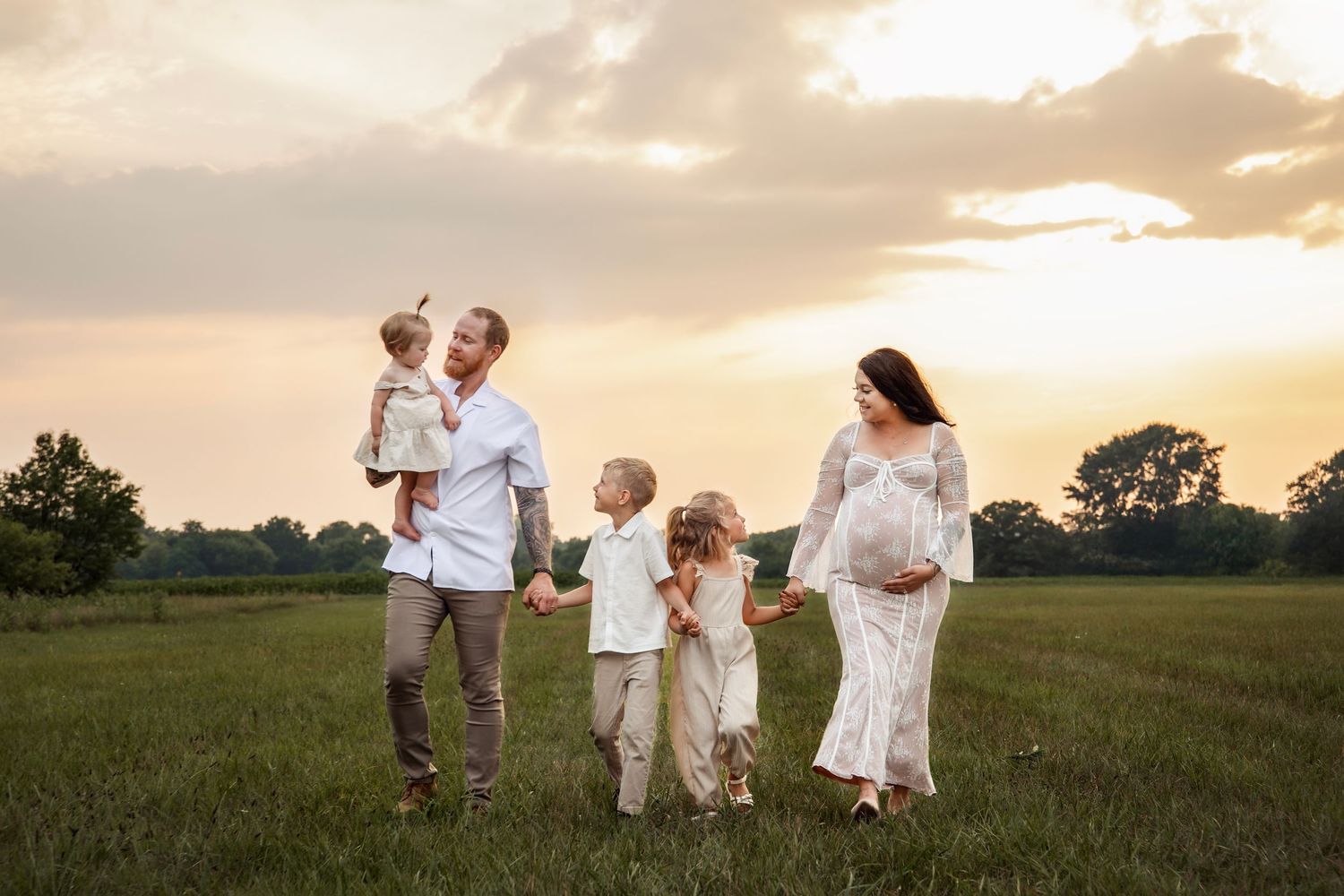 A group in white clothing stands in a golden field during sunset as their shadows stretch across the landscape.