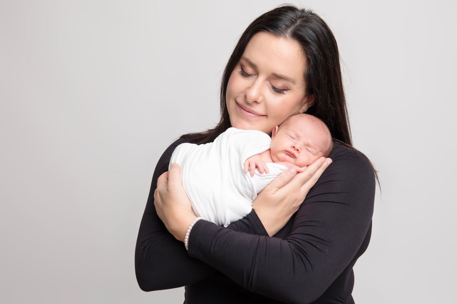 Tender newborn photography session showing parent in black shirt cradling sleeping baby in white.