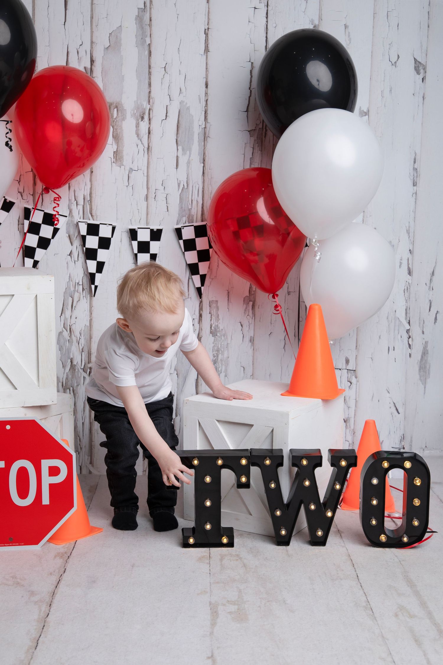 A toddler plays with race-themed party decorations featuring balloons and checkered flags.