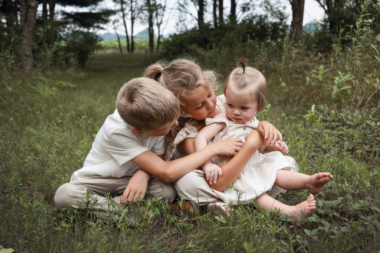 Three children sitting together on grass in an outdoor setting sharing a sweet moment.