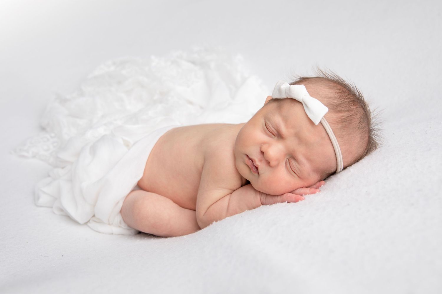 Peaceful newborn sleeping under delicate white lace wrap in soft light.