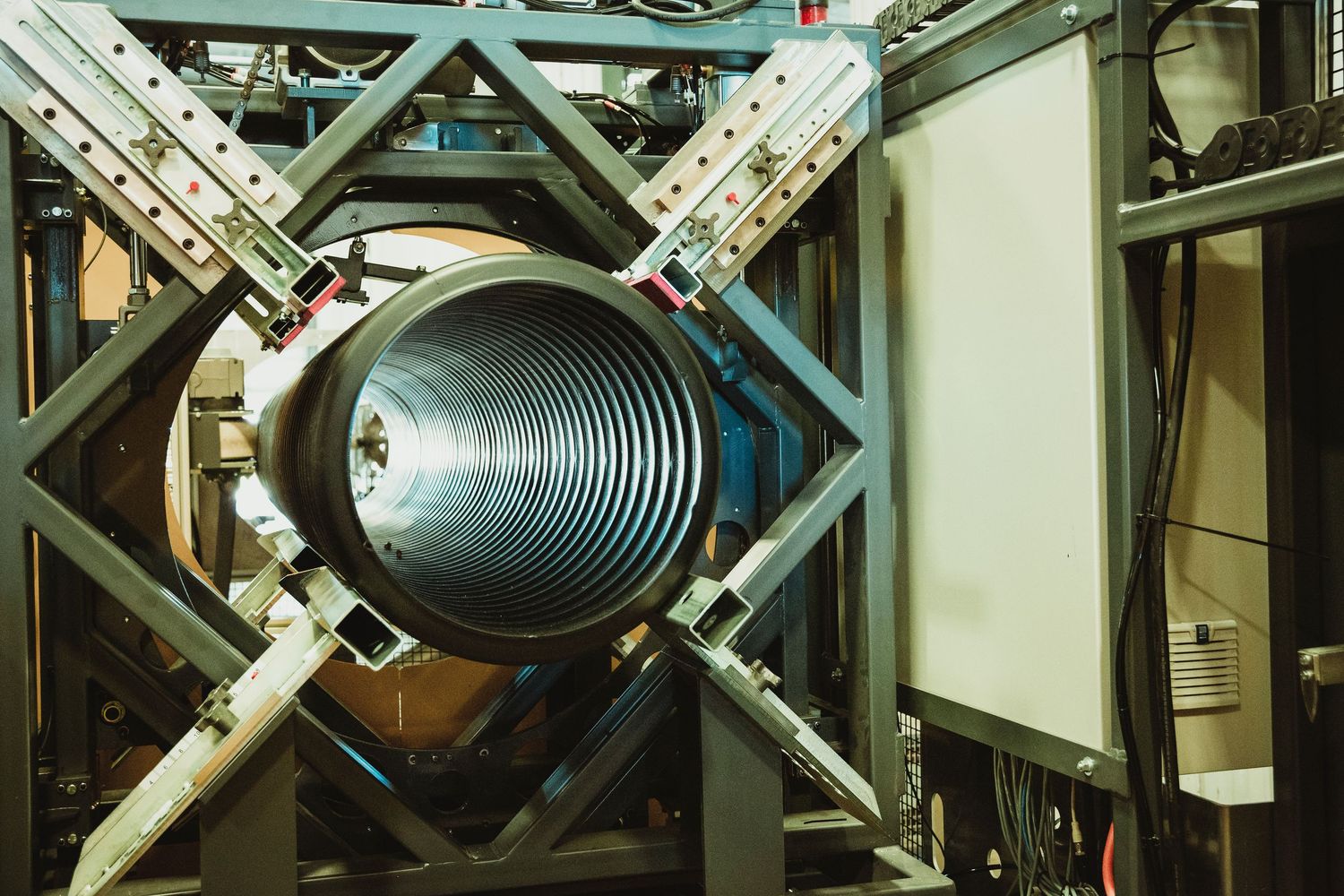 Large industrial spiral pipe or tube supported by metal framework and equipment in manufacturing facility.