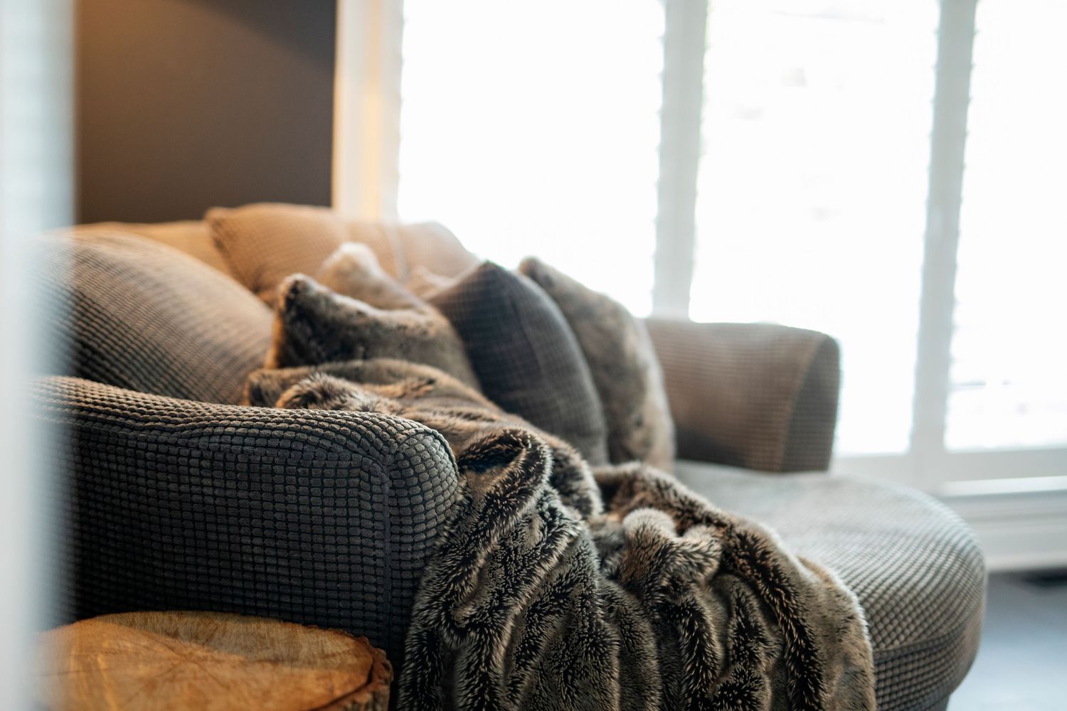 A cozy gray couch with soft blanket and pillows next to a bright window in a living room.