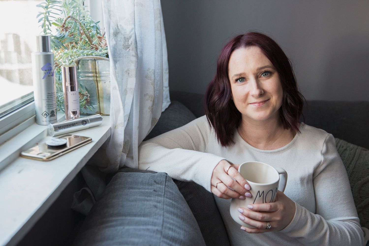 Person in cream colored sweater sitting by window drinking from mug on cozy winter morning.
