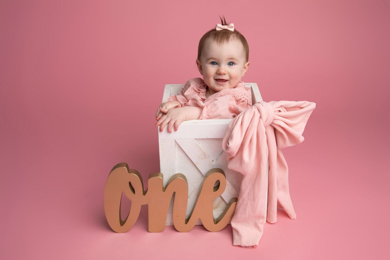 Seven milestone photos of a baby's first year growth journey against a pink backdrop with monthly markers and bows.