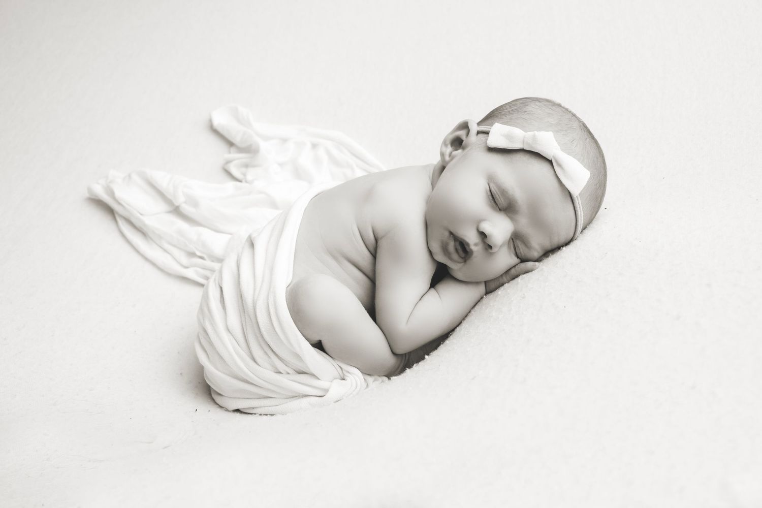Artistic black and white portrait of sleeping newborn wrapped in white fabric.