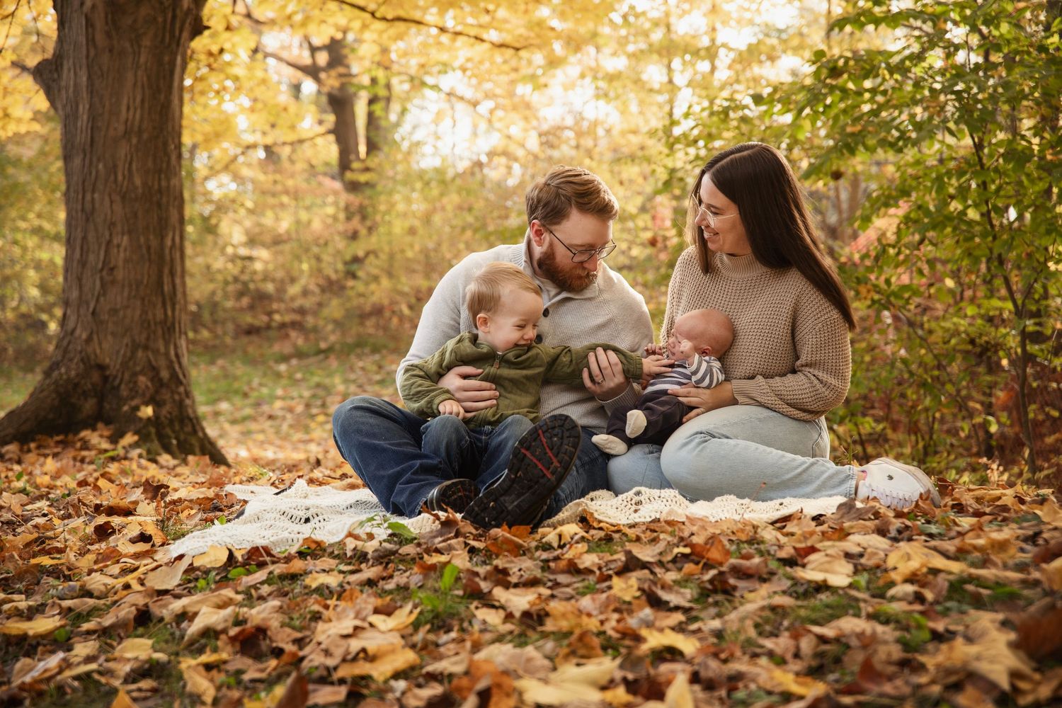 Family having a cozy fall picnic on golden leaves in a wooded setting.