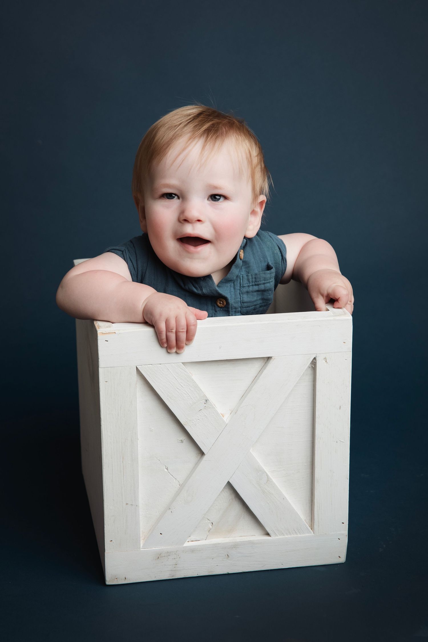 Studio photos of a small child sitting in a white wooden box against a dark navy blue background.