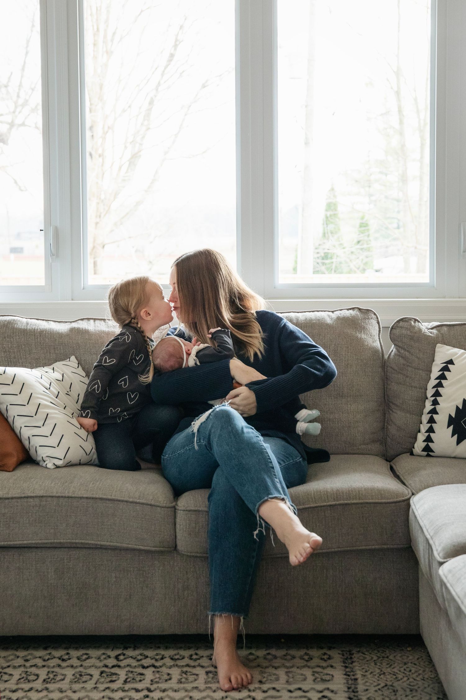 Sweet candid moment between parent and child cuddling on grey sectional sofa near windows.