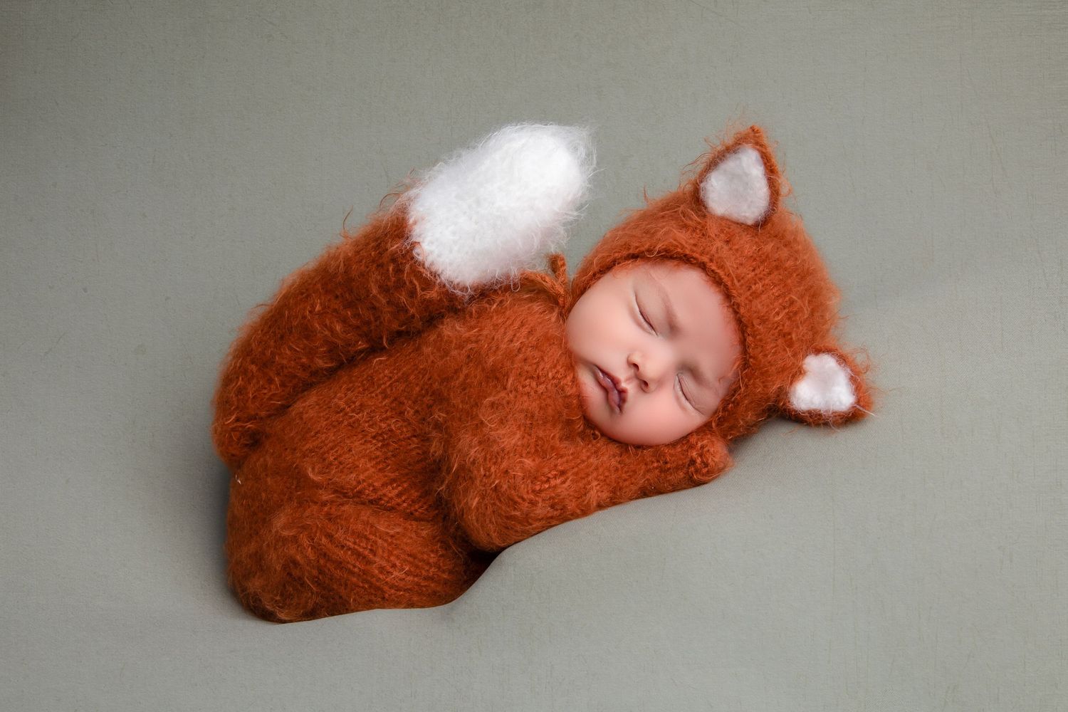 Sleeping newborn wearing adorable fox costume with ears and tail.