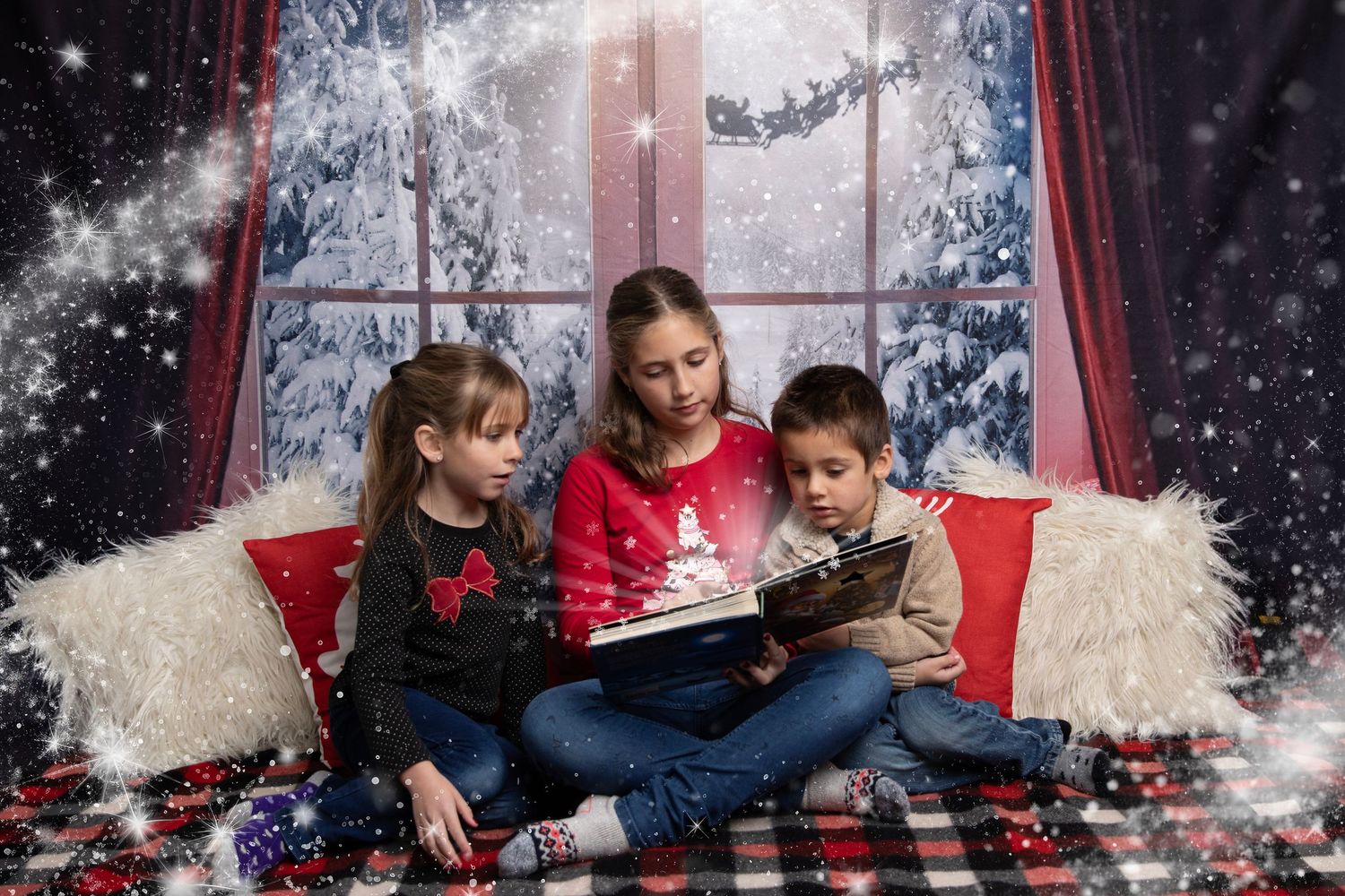 Family sits together on a plaid blanket in front of a snowy window backdrop during a winter photo session.