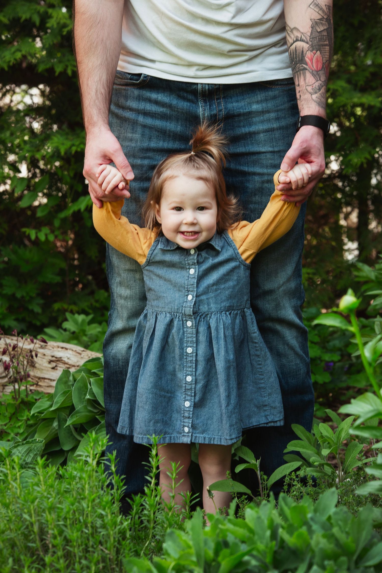 Close-up shots of toddler in denim dress holding hands in garden setting.