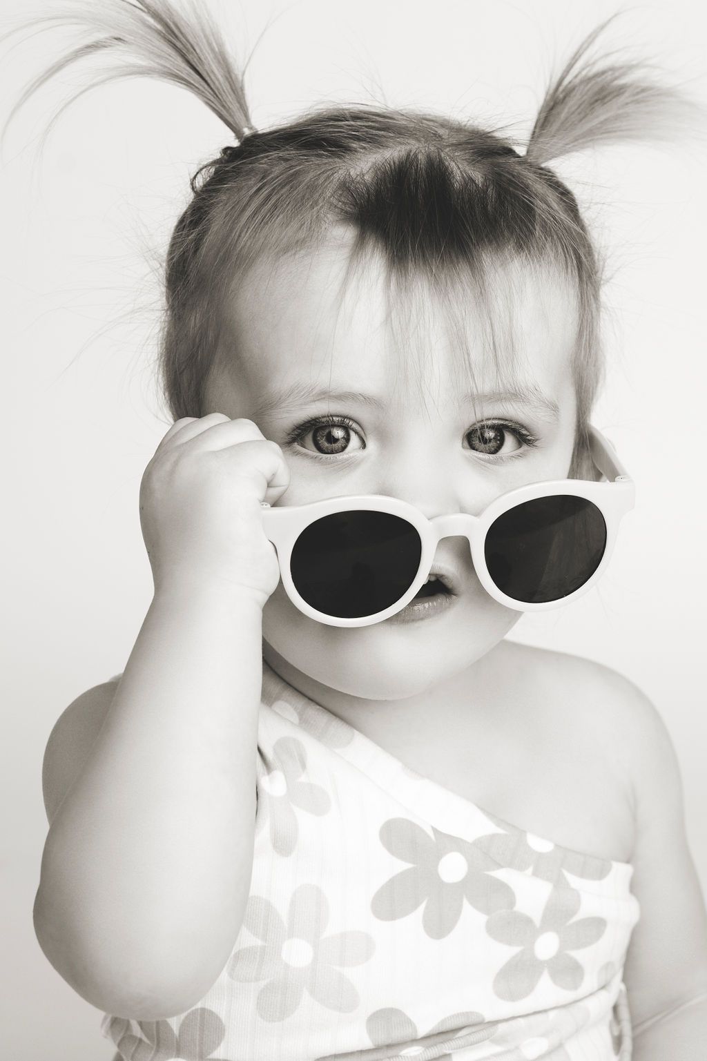 Collection of black and white photos showing a small child wearing sunglasses and flowered dress.