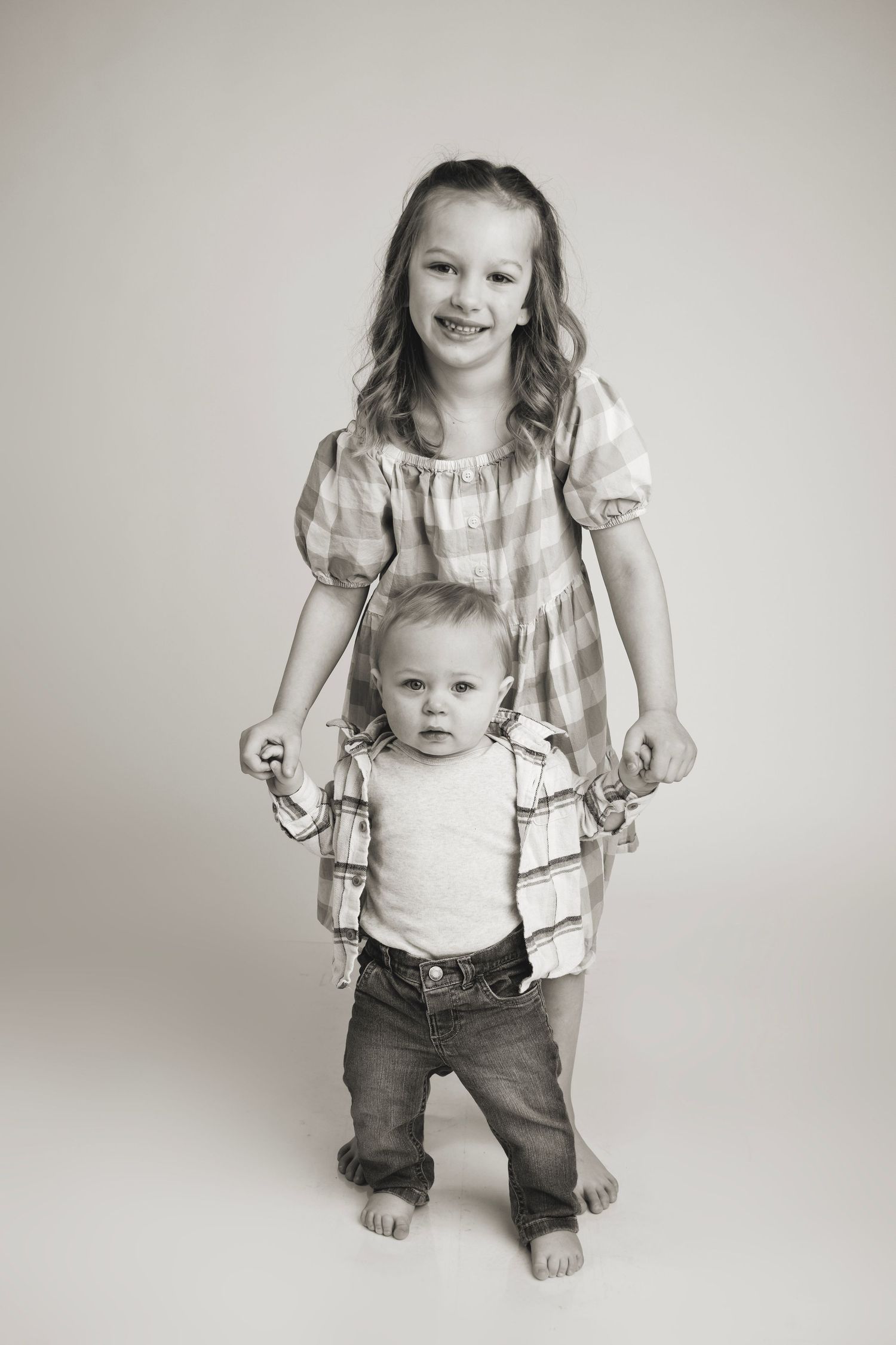 Siblings posing together for black and white portrait against studio background.