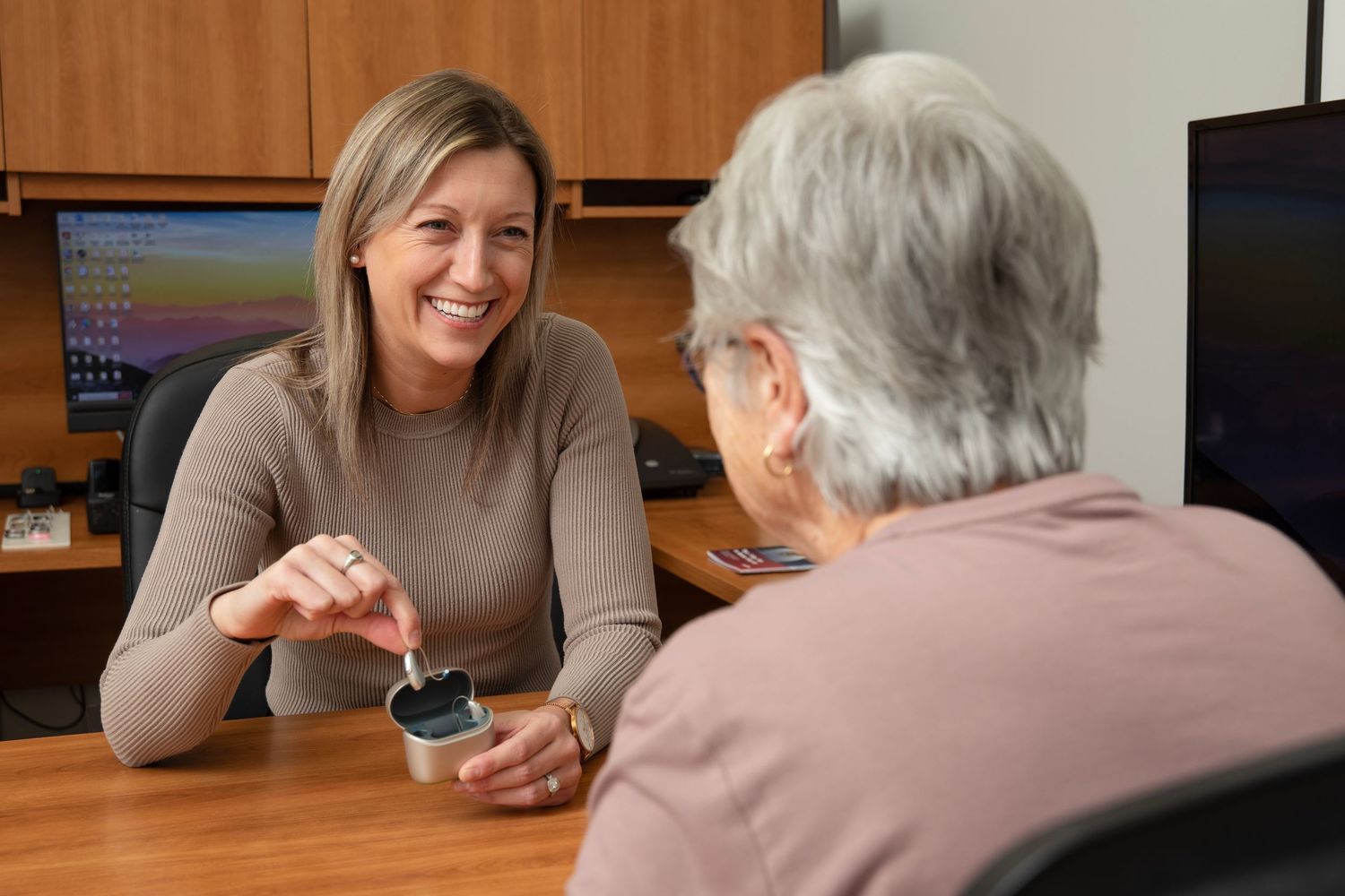 Two people sit across from each other at a wooden table having a conversation in a home setting.