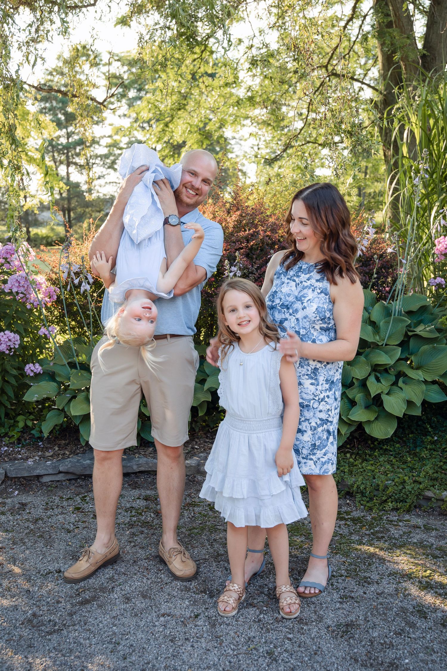 Family enjoying playful outdoor photoshoot in garden with blooming flowers and greenery.
