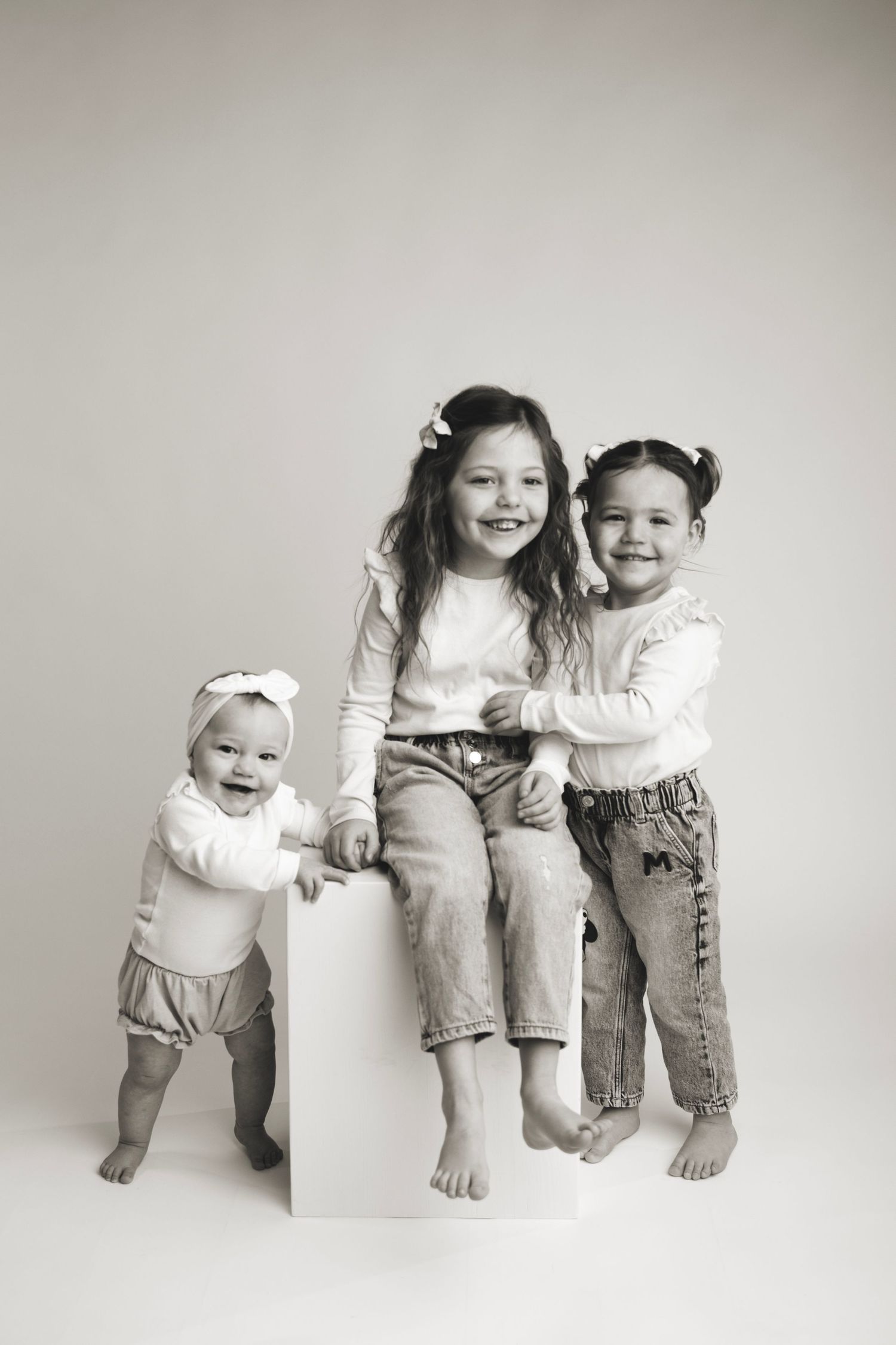 Sweet black and white photo collage showing three siblings sitting together, posing and playing in various arrangements.