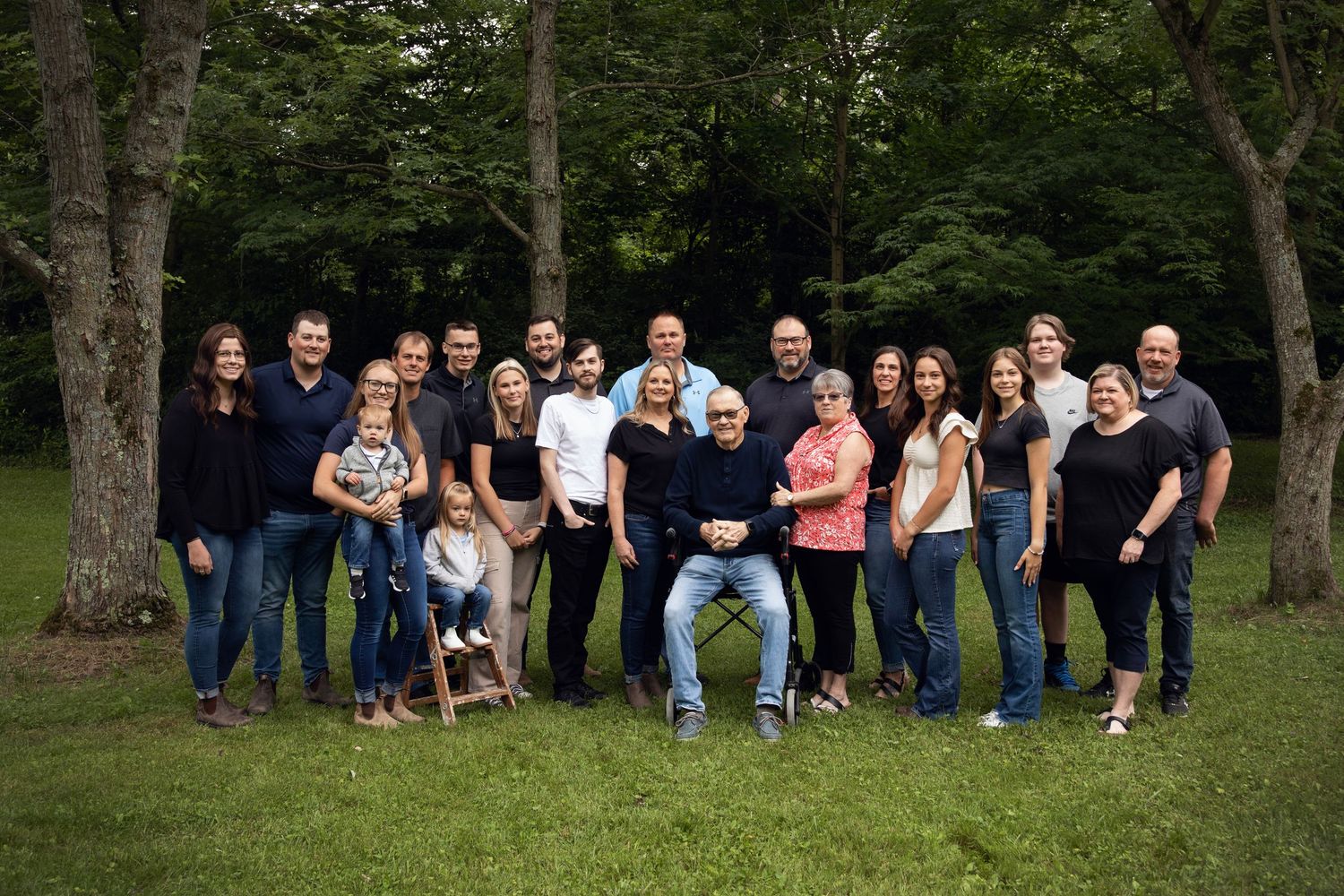 Large extended family group poses outdoors for portrait in summer park setting.