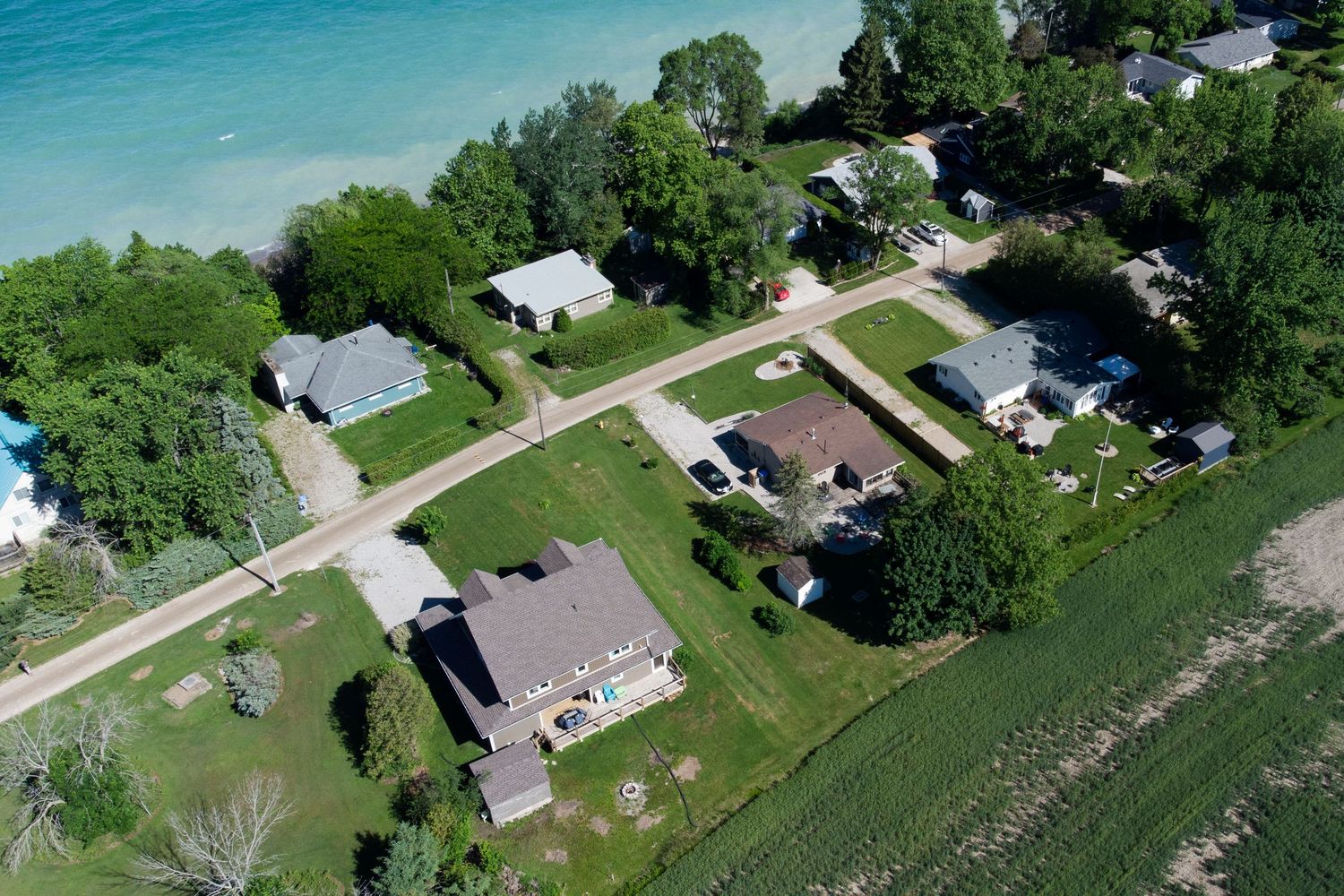 Aerial view of lakeside homes and cottages with manicured lawns along turquoise water on a summer day.