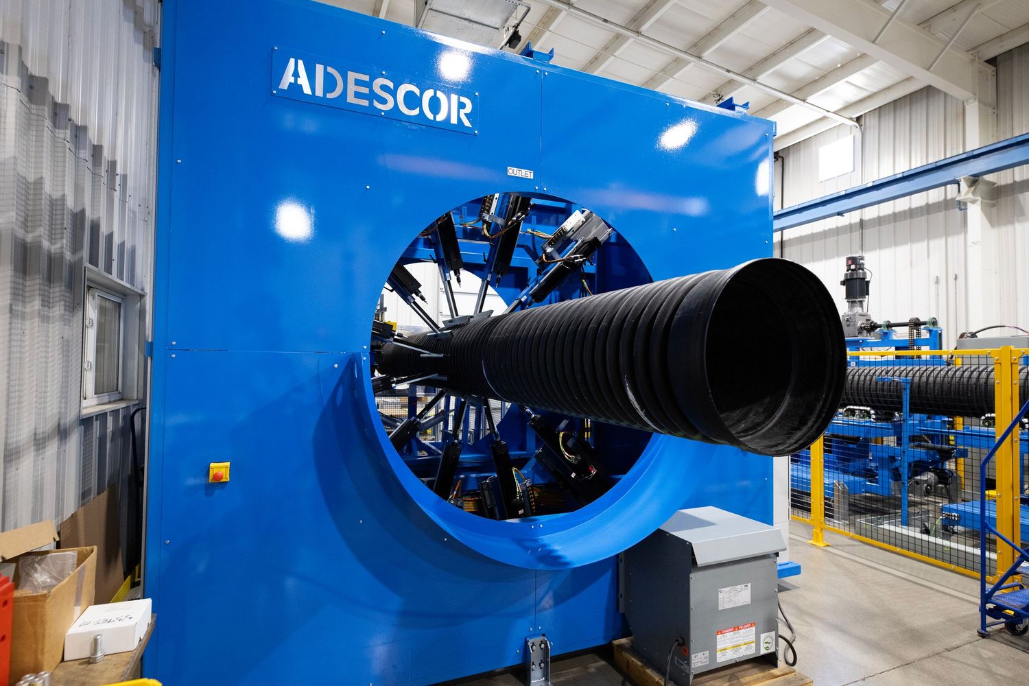 Large blue industrial pipe extrusion machine with circular opening in manufacturing facility.