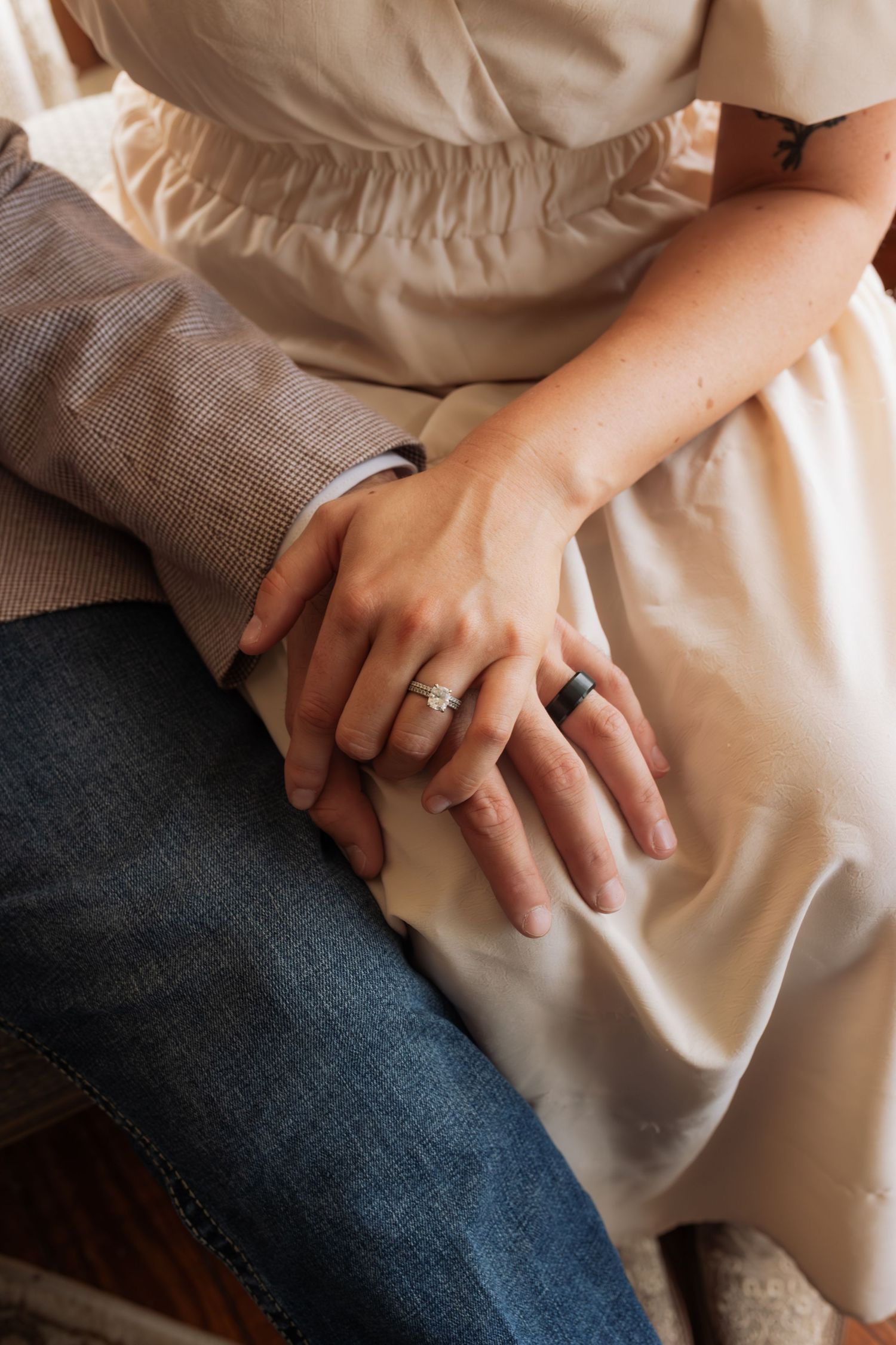 Close-up of couple's hands showing engagement and wedding rings, bride in cream dress, groom in plaid jacket.