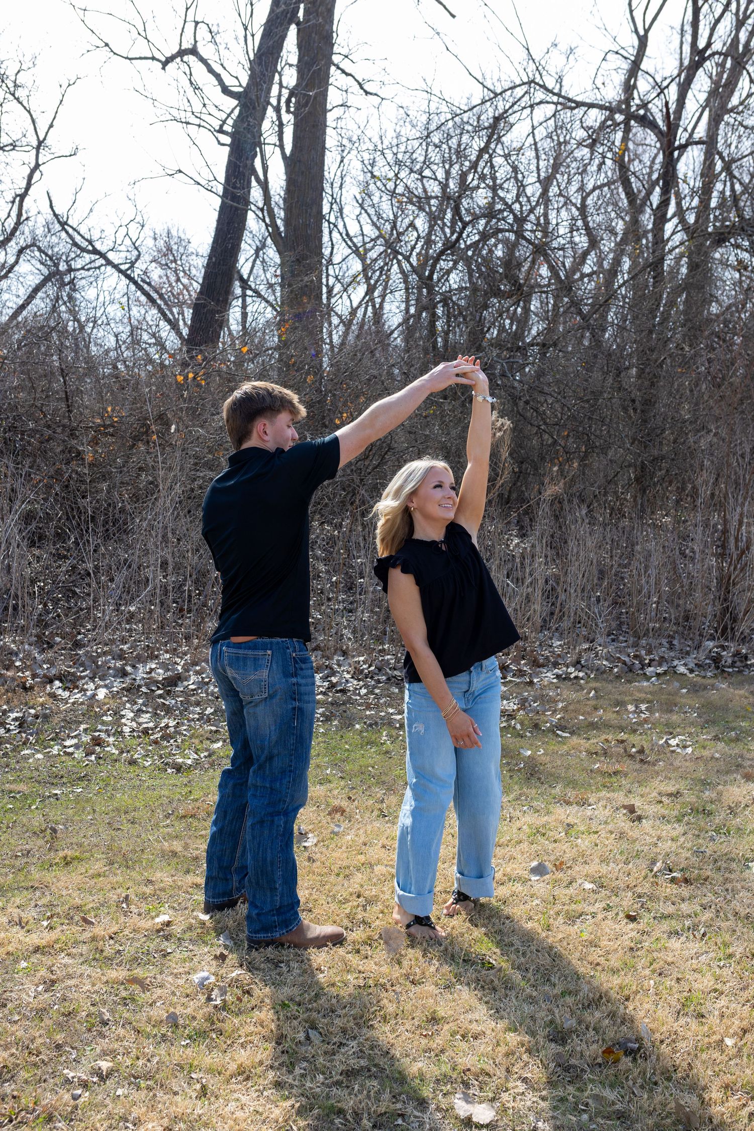 Couple dancing together in casual attire against a winter forest backdrop.