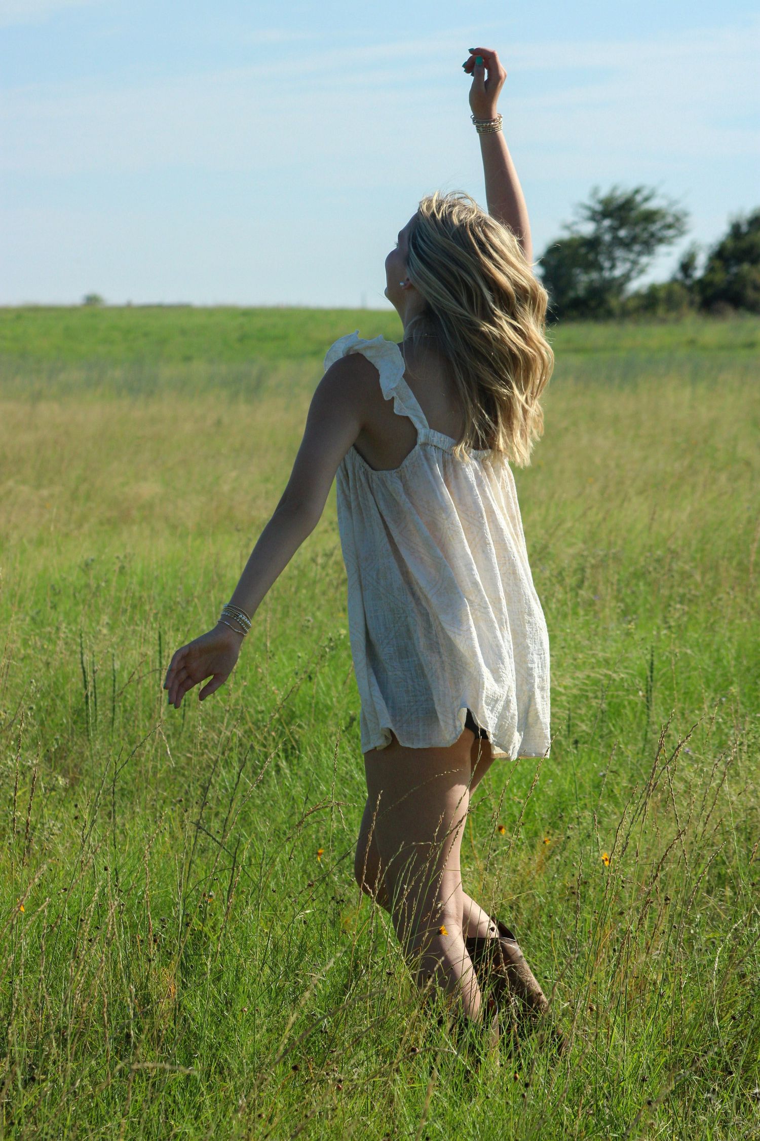 Person in white dress dancing through tall grass field.