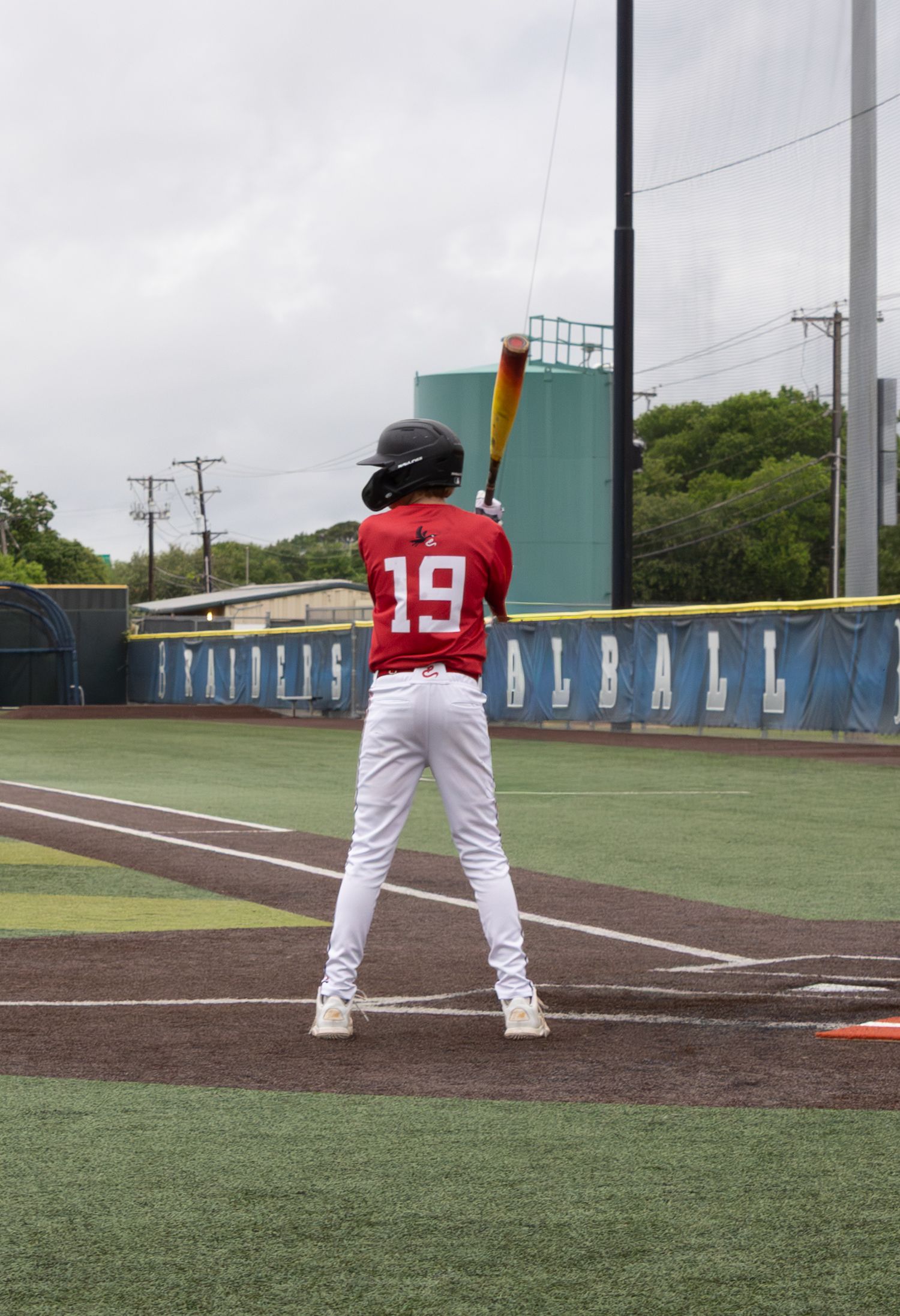 Baseball player #19 in red uniform stands at bat on a green field, ready to swing during a game.