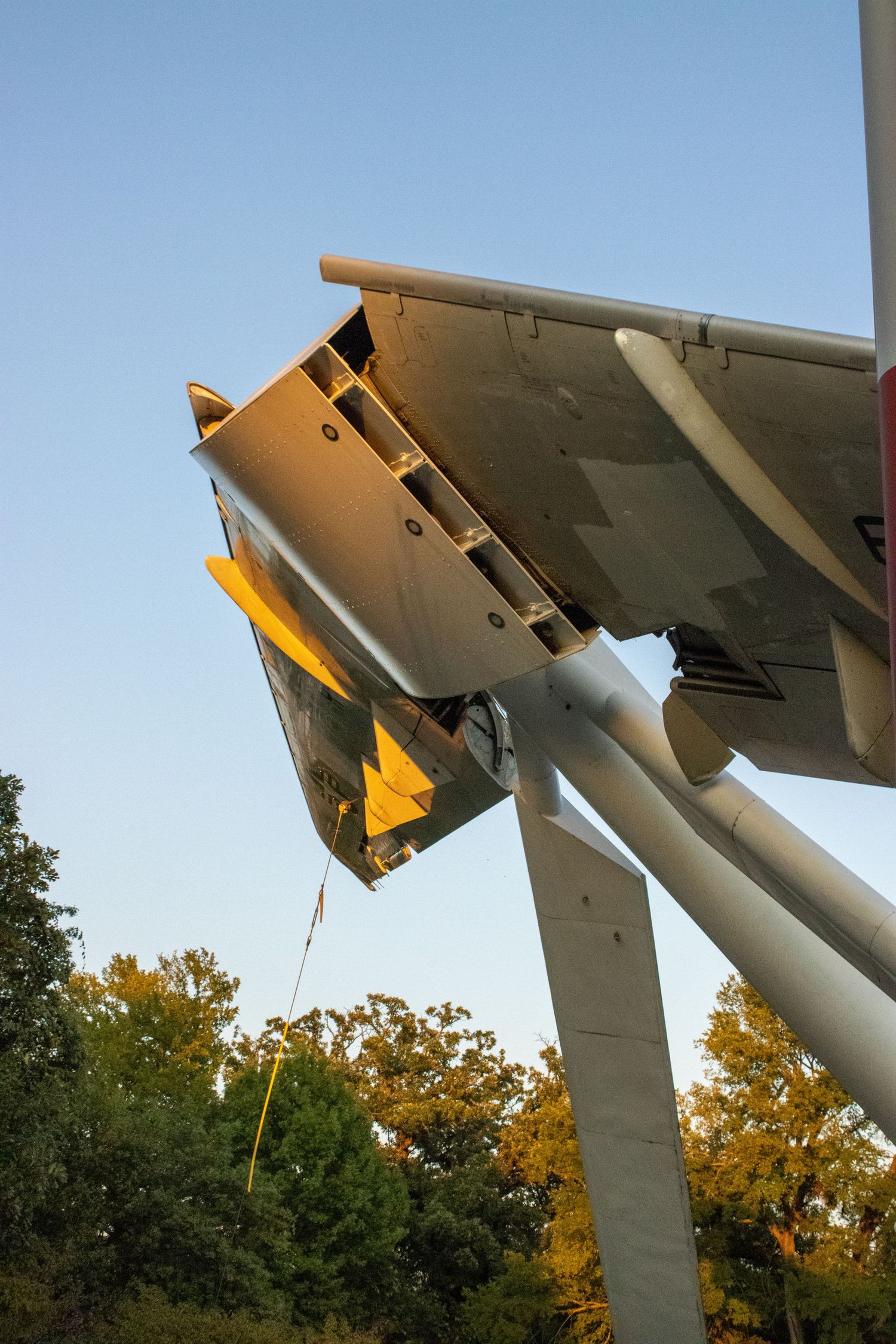 Close-up of military aircraft weaponry mounted under a wing at sunset.