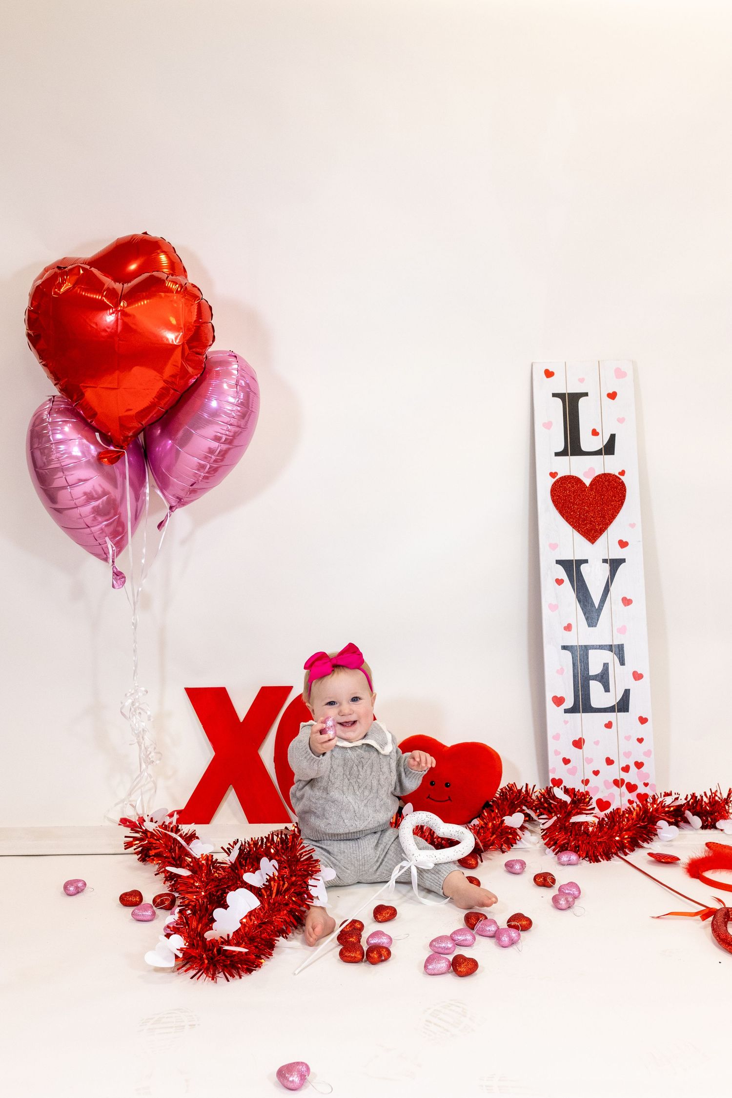 Valentine's day themed photo setup with red heart balloons, LOVE sign, and festive decorations against white background.