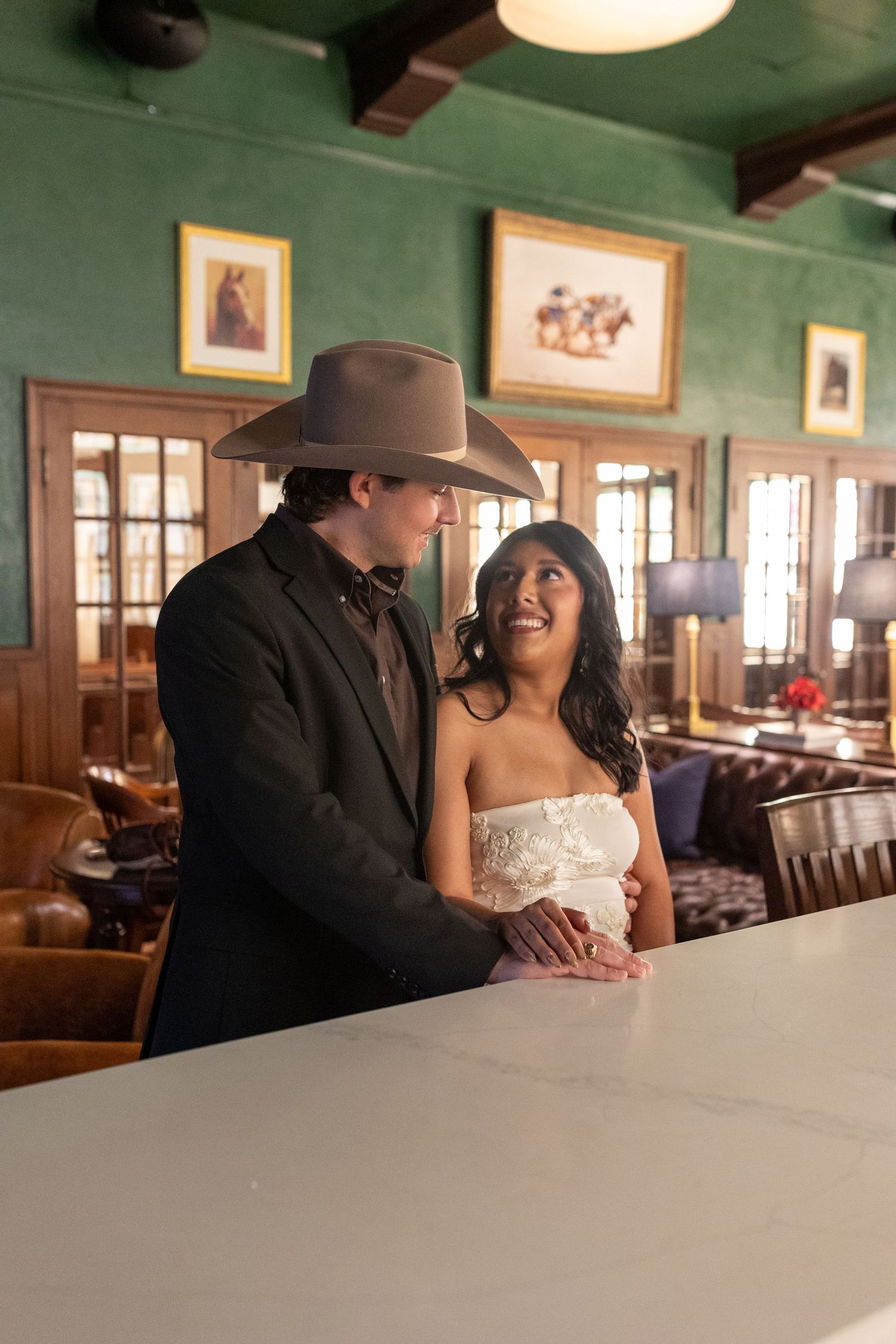 A couple in western attire shares intimate moments in a rustic restaurant setting with wood paneling and framed artwork.