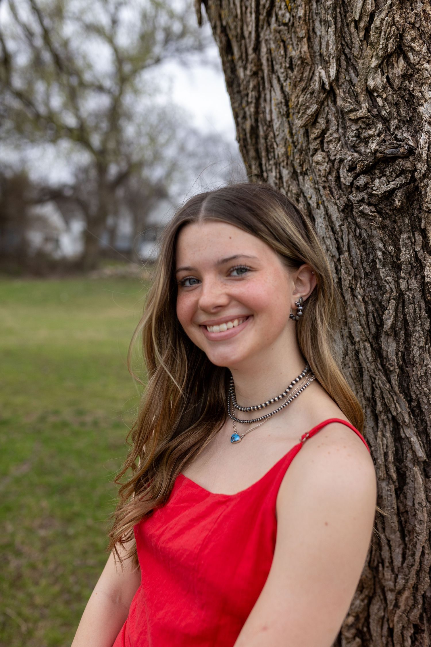 A series of outdoor portraits in front of a tree trunk showing someone wearing a sleeveless red dress.