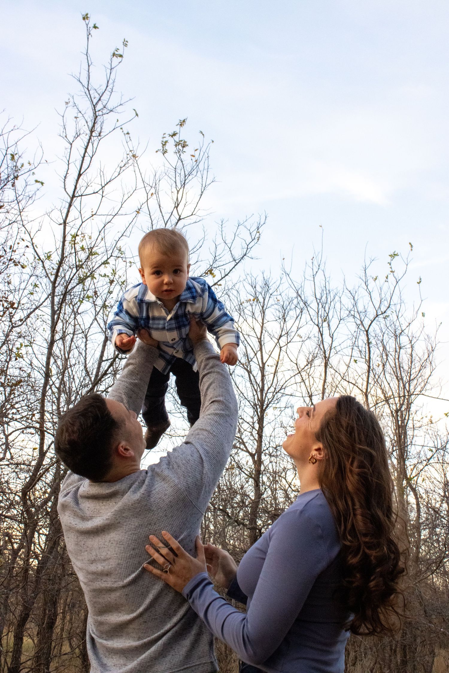 A sequence of four photos showing a joyful moment outdoors with a baby being lifted up against a backdrop of bare trees.