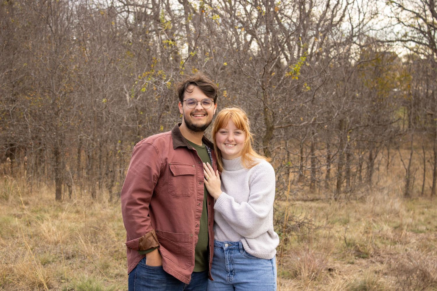 A couple shares tender moments in a wooded autumn setting during an outdoor photo session.