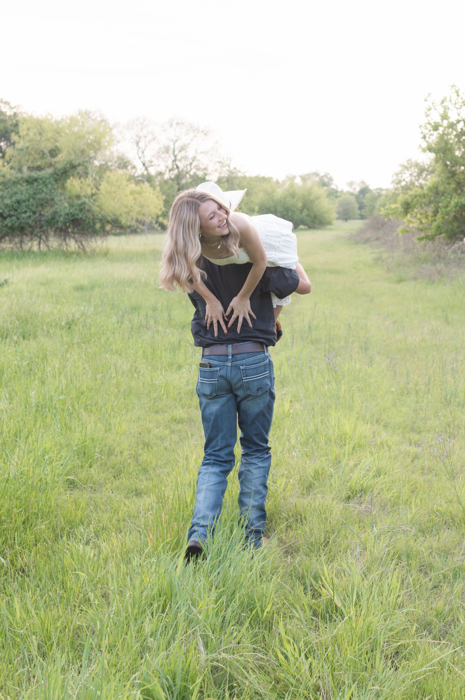 Couple sharing a joyful piggyback ride in a lush green meadow surrounded by trees.